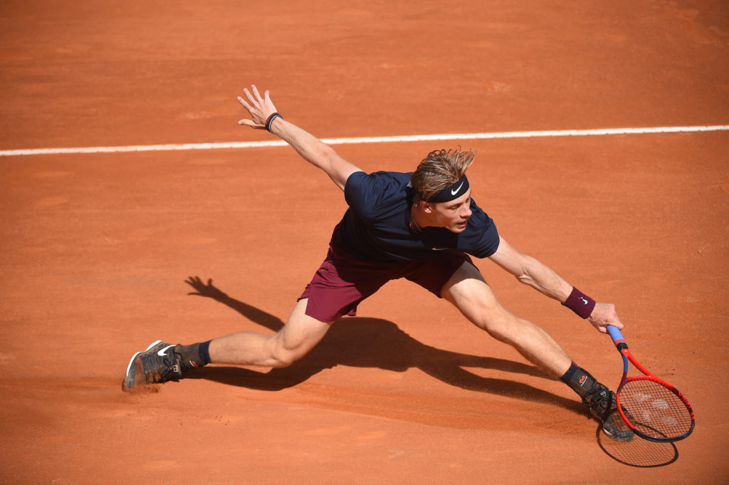 Shapovalov slides to hit a low backhand slice on a clay court