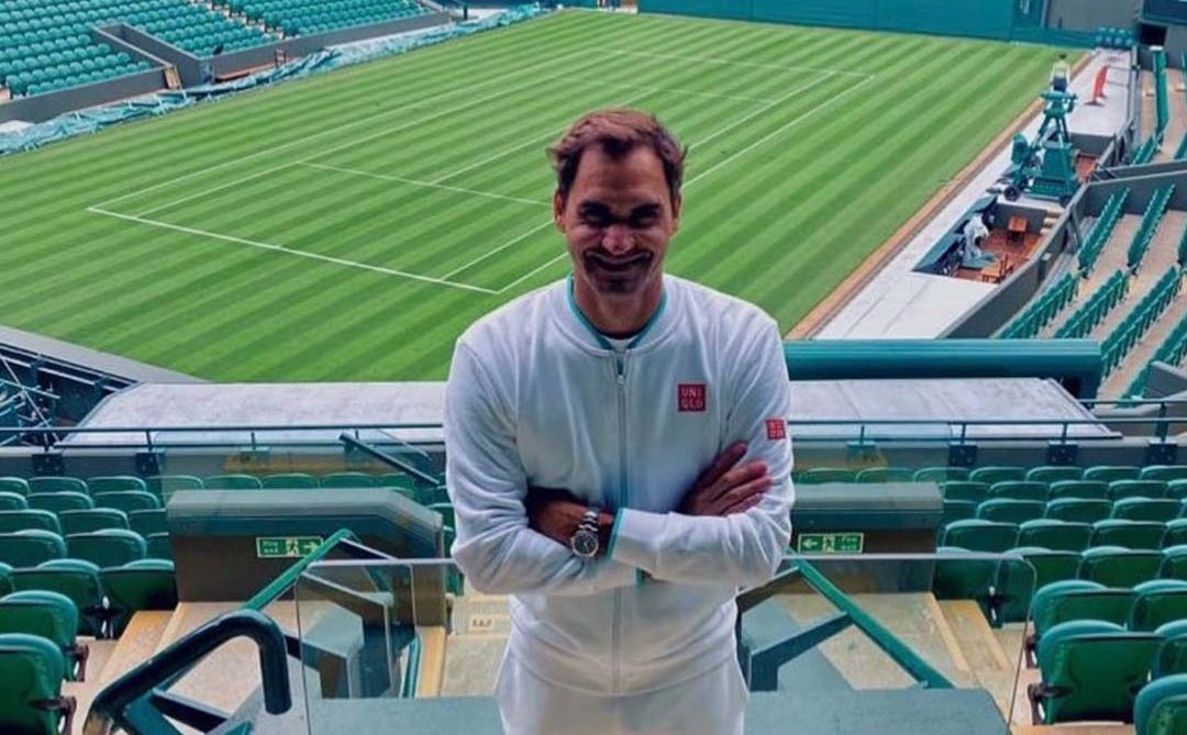 Roger Federer standing in front of the Centre Court at Wimbledon and smiling to the camera