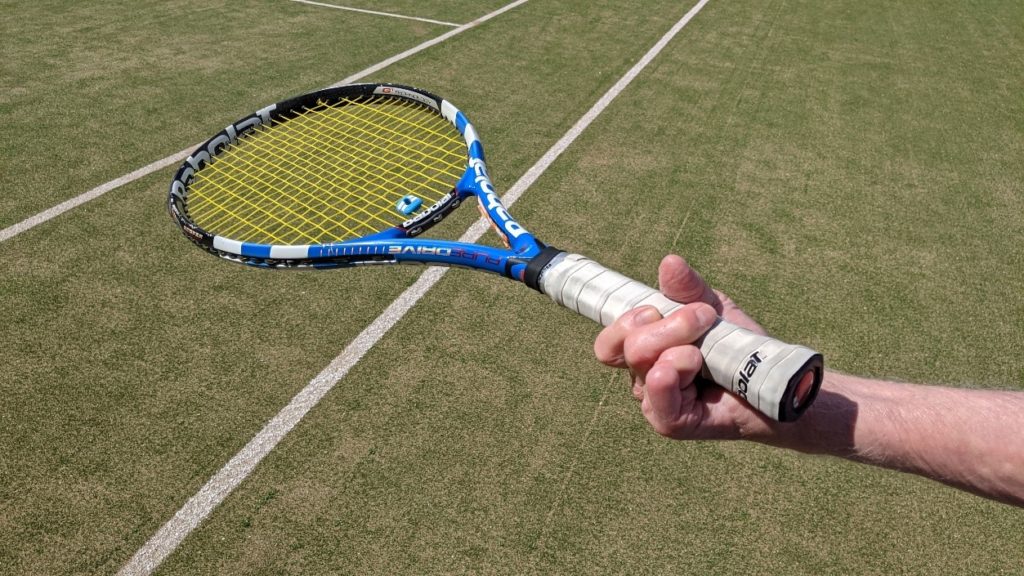 A hand missing two fingers holds a tennis racket