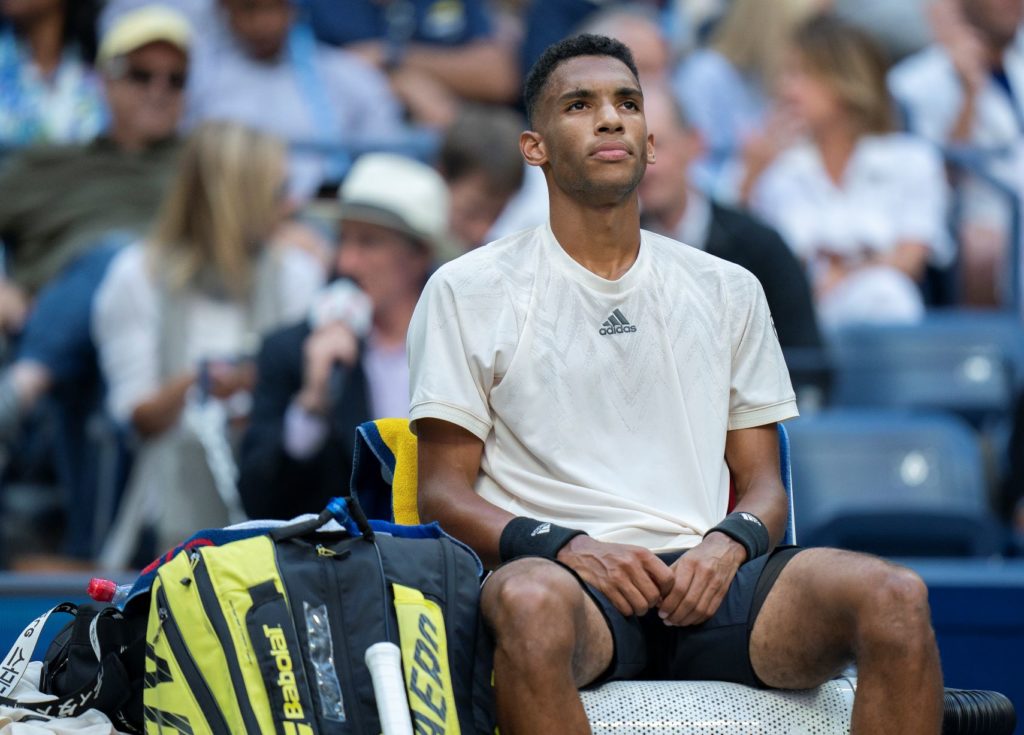 Felix Auger-Aliassime sits in his chair and stares off into the distance.