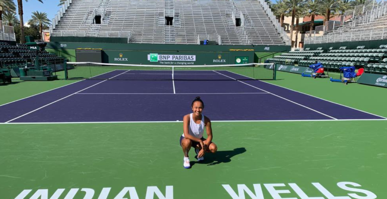 Leylal Fernandez kneels just above the Indian Wells sign on a court.