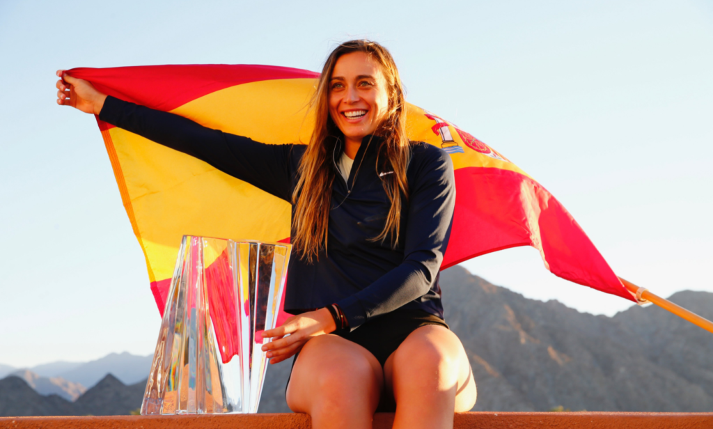 Paula Badosa sits next to the trophy and waves the Spanish flag.