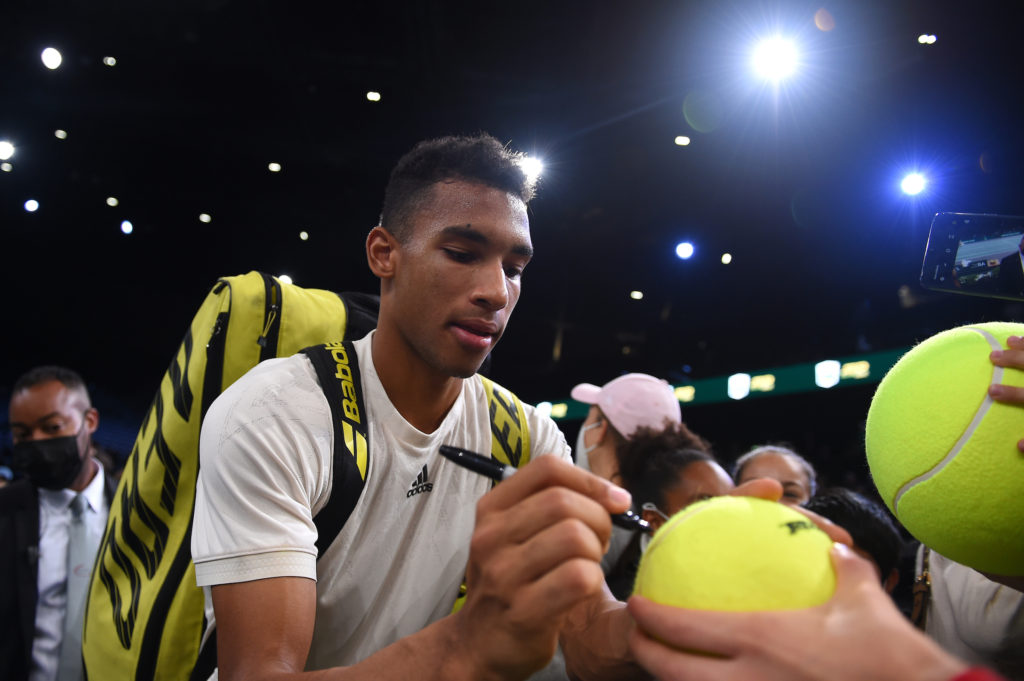 Felix Auger Aliassime signs tennis balls for fans after a match