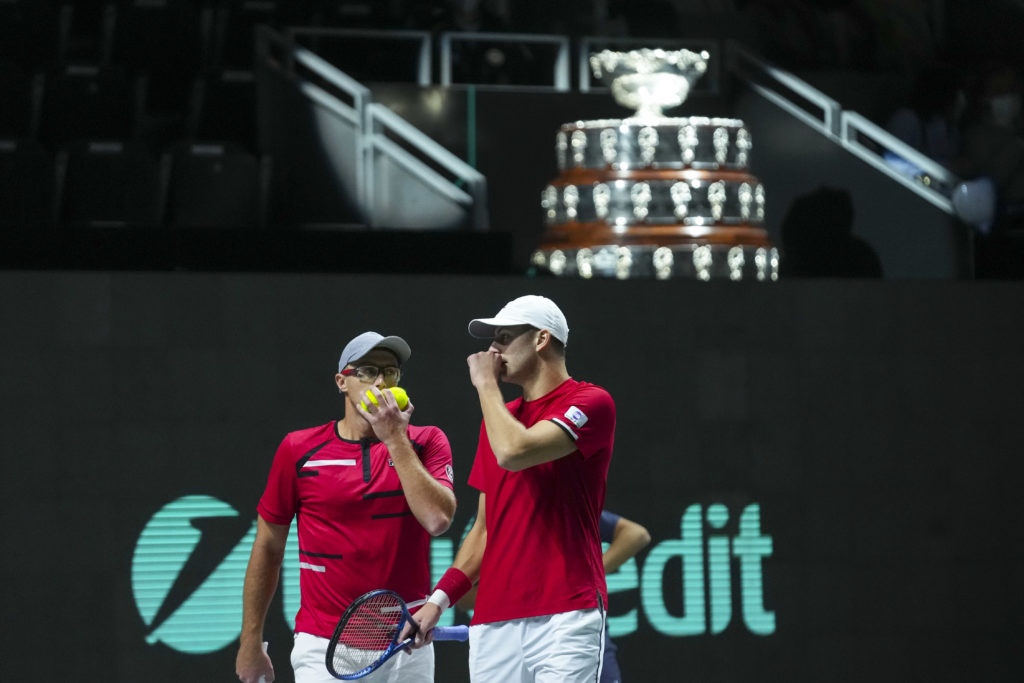 Peter Polanksy and Brayden Schnur whisper to each other in front of the Davis Cup Trophy.