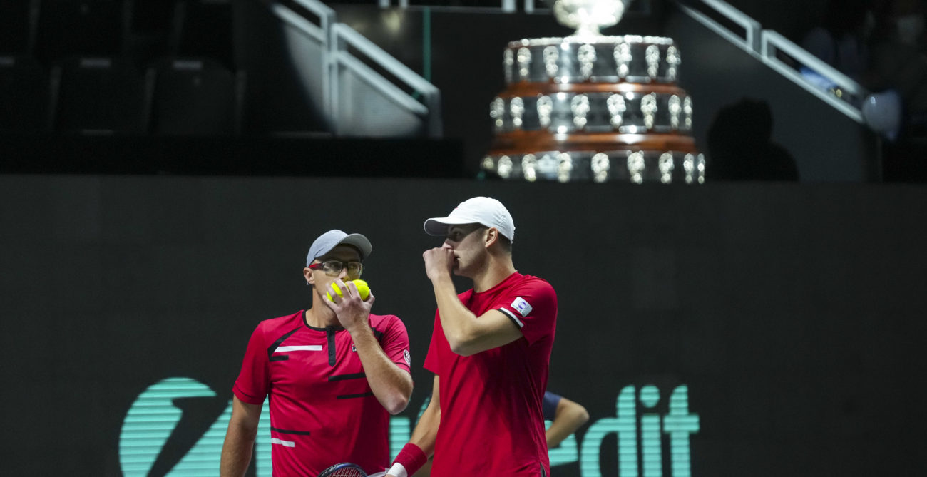 Peter Polanksy and Brayden Schnur whisper to each other in front of the Davis Cup Trophy.