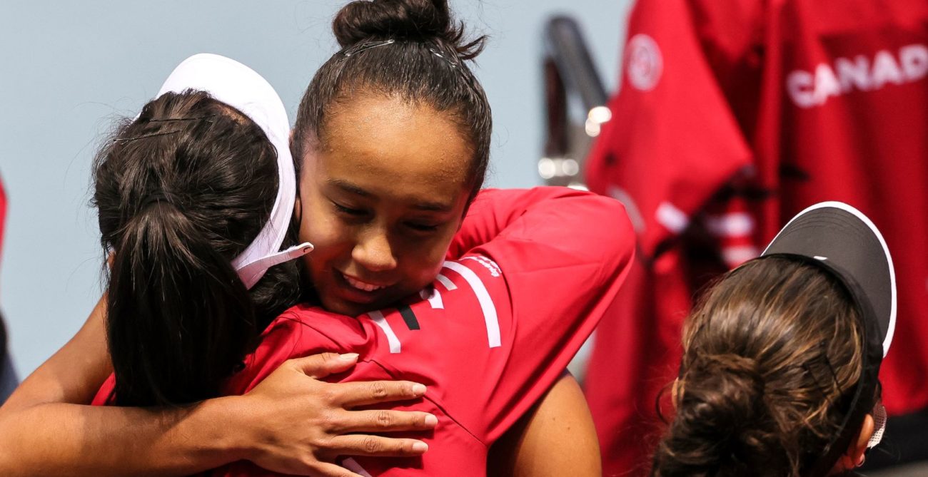 Leylah Fernandez hugs a person wearing a red jacket with Cnada written on it after a Billie Jean King Cup match
