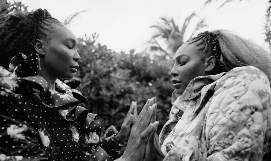 Venus and Serena Williams face each other and hold hands.