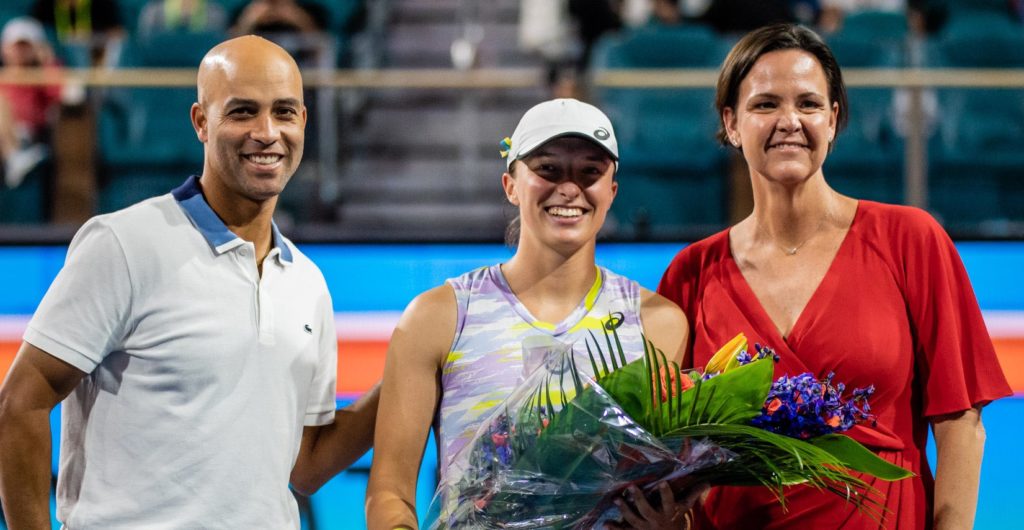 James Blake, Iga Swiatek and Lindsey Davenport stand on the court and smile.