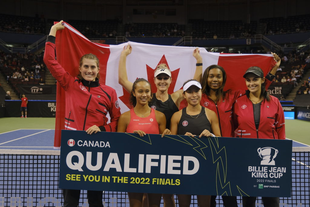 Team Canada stands behind the net holding a sign that reads "qualified" while holding the flag behind them.