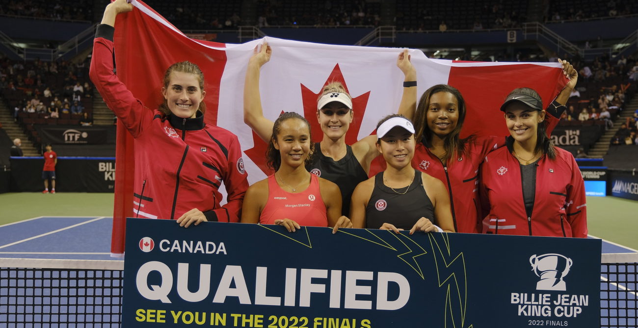 Team Canada stands behind the net holding a sign that reads "qualified" while holding the flag behind them.