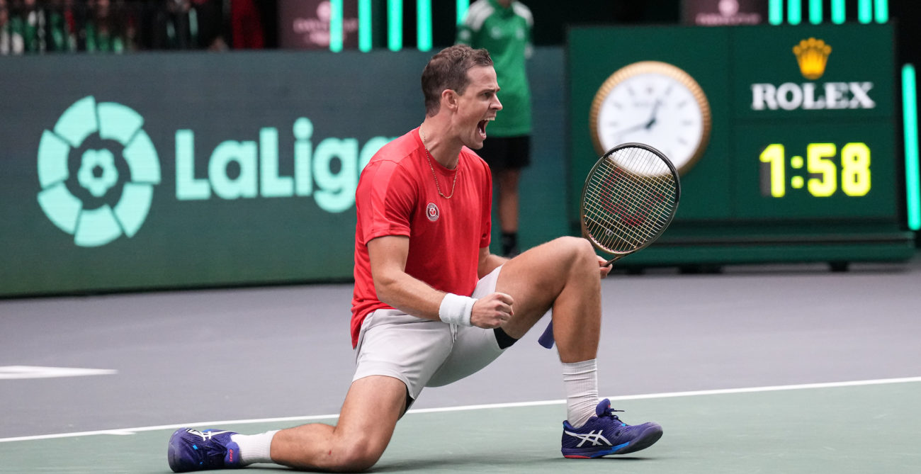 Vasek Pospisil kneels on the court, pumps his fist and shouts.