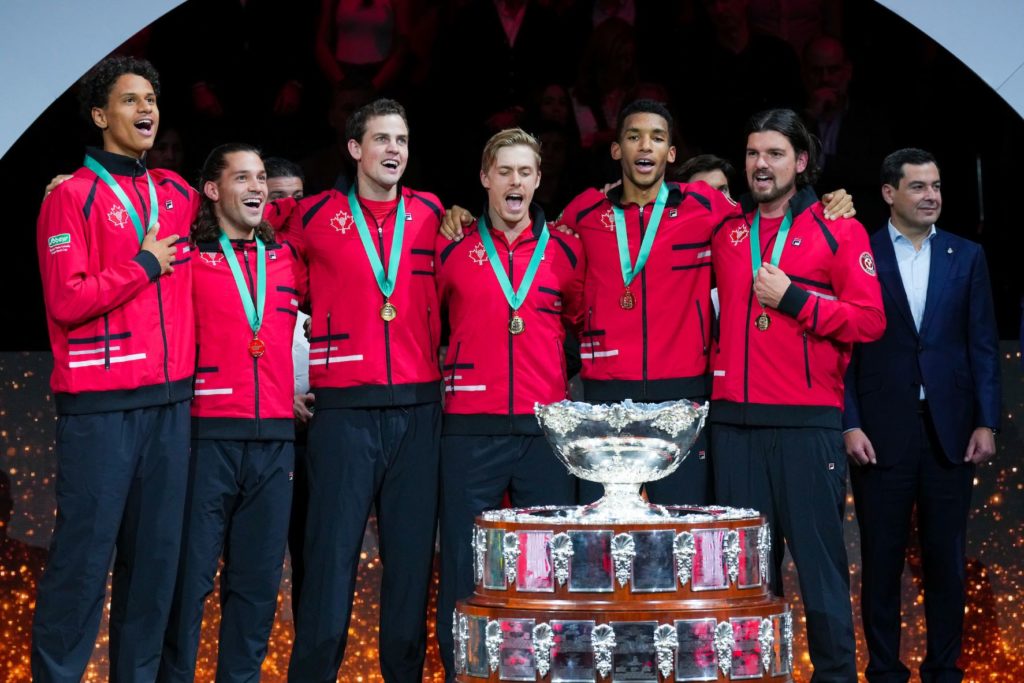 From left to right, Gabriel Diallo, Alexis Galarneau, Vasek Pospisil, Denis Shapovalov, Felix Auger-Aliassime and Frank Dancevic stand behind the Davis Cup trophy and sing O Canada