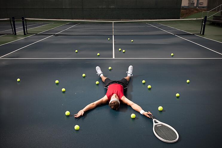 Stock photo of tennis player lying down on the court surrounded by tennis balls