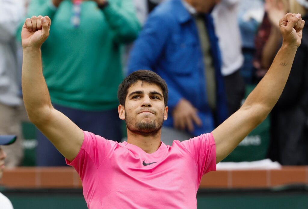 Carlos Alcaraz raises his fists above his head in triumph.