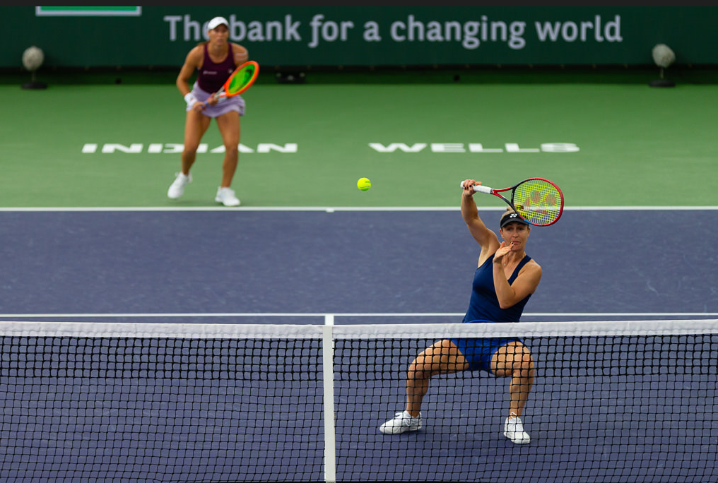 Gabriela Dabrowski crouches low behind the net to hit a volley over her head.