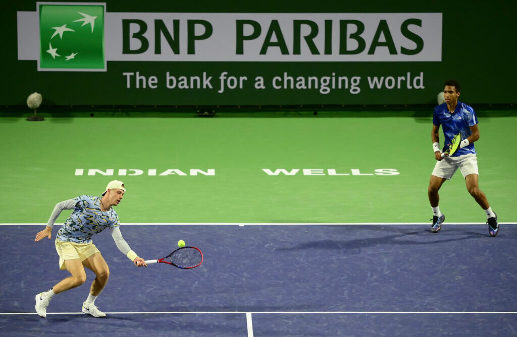 Denis Shapovalov (left) hits a volley as Felix Auger-Aliassime stands near the baseline.