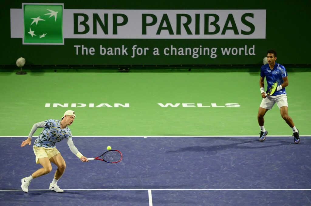 Denis Shapovalov (left) hits a volley as Felix Auger-Aliassime stands near the baseline.