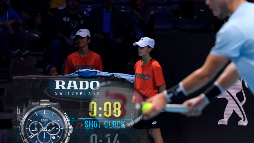 A player prepares to serve with the shot clock visible in the background.