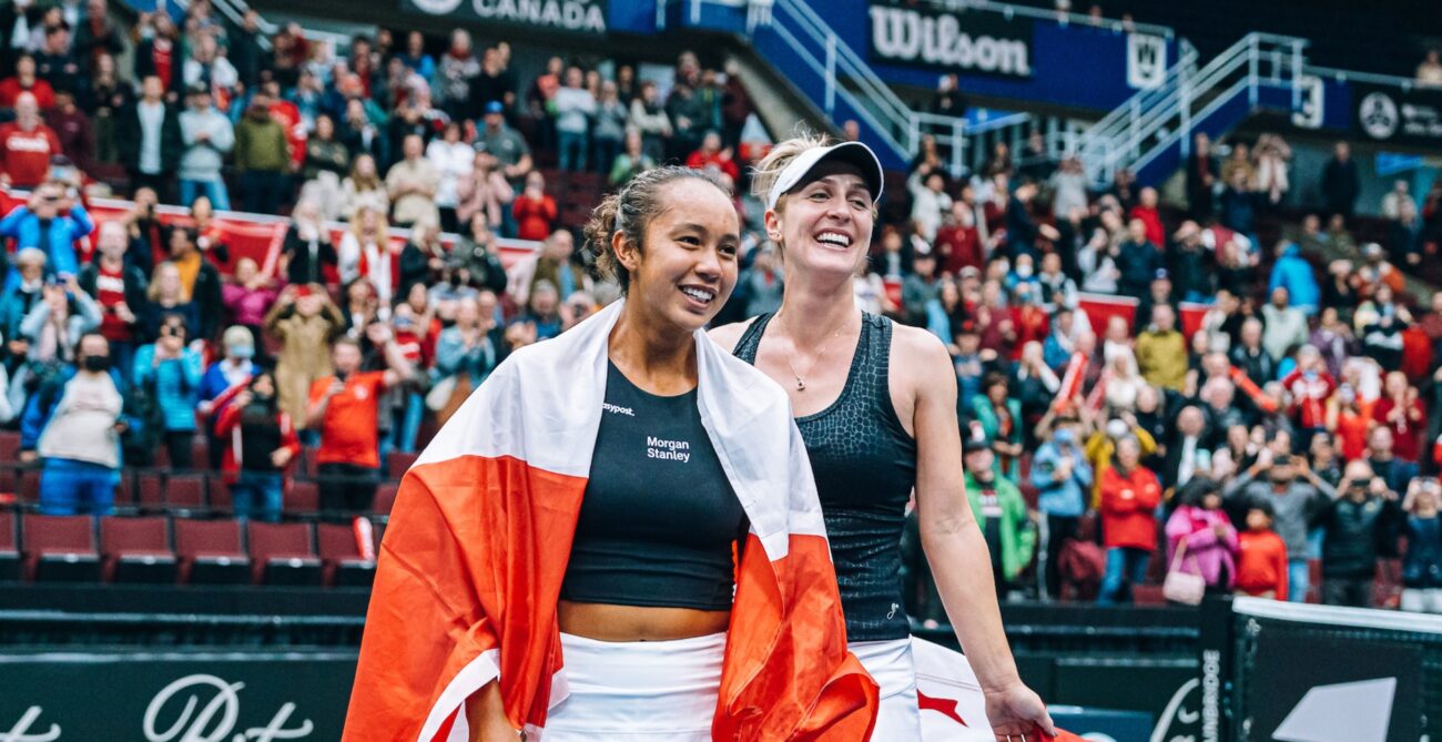Leylah Fernandez (left) and Gabriela Dabrowski smile on court holding Canadian flags.