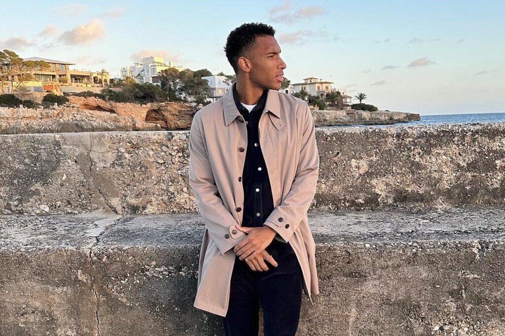 Felix Auger-Aliassime leans on a rock outdoors.