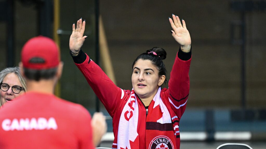 Bianca Andreescu stands on the Canadian bench and raises her hands over her head.
