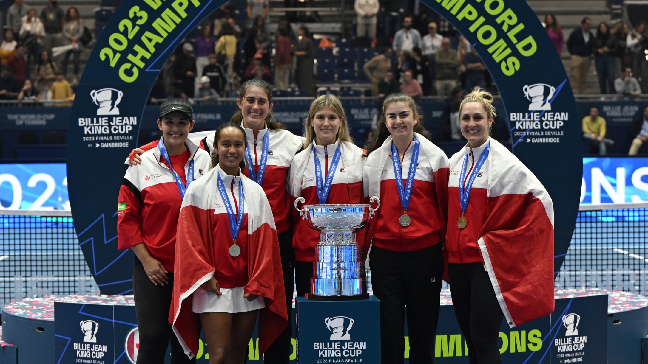 From left to right, Heidi El Tabakh, Leylah Fernandez, Rebecca Marino, Eugenie Bouchard, Marina Stakusic, and Gabriela Dabrowski wear their medals and stand behind the Billie Jean King Cup trophy, the World Cup of Tennis.