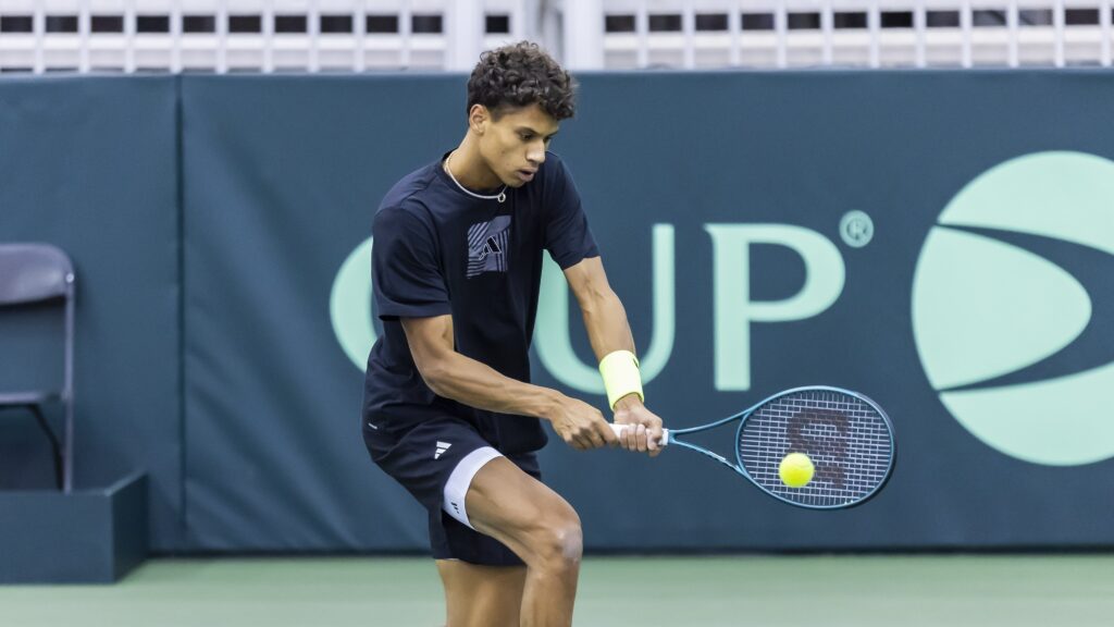 Gabriel Diallo hits a backhand in front of the Davis Cup sign.